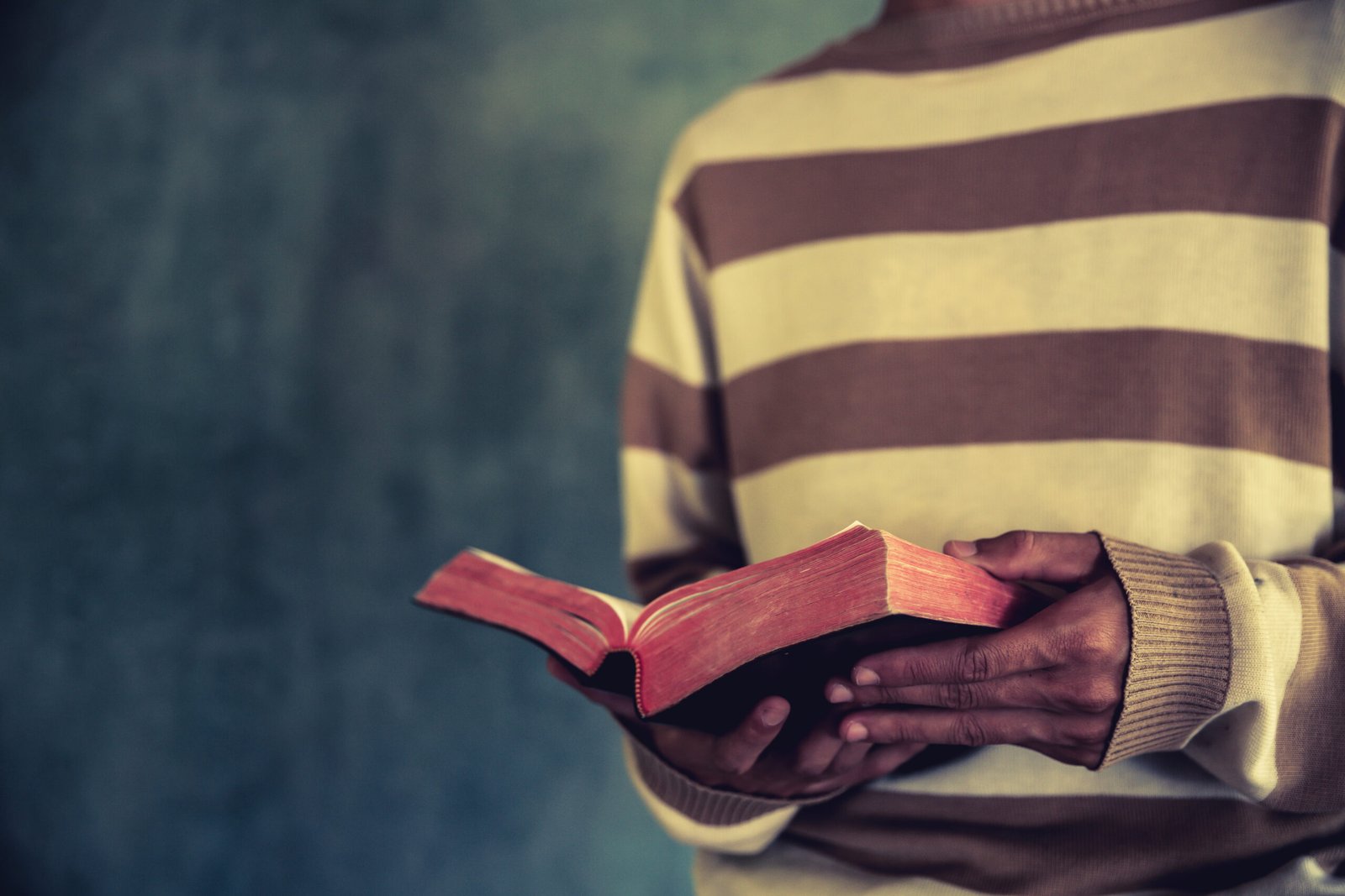 a man standing while reading bible or book over concrete wall with window light